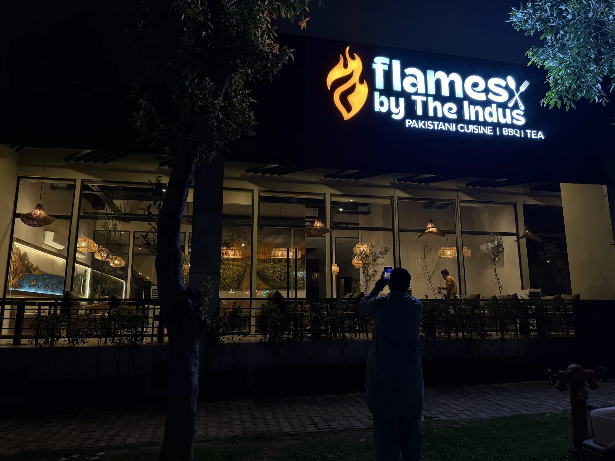 The Flames by the Indus frontage at night, the dining room lit behind the glass